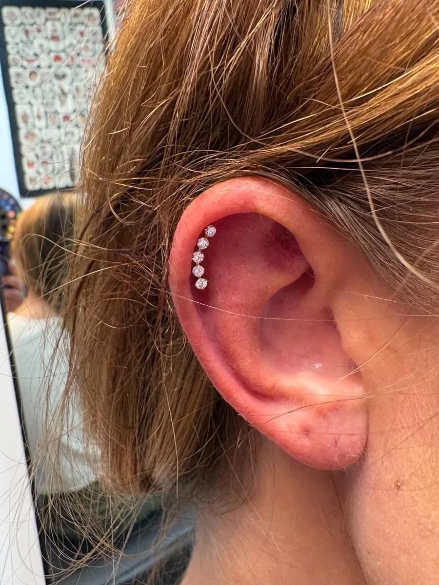 Five crystal helix studs stacked along the upper ear cartilage, hair pinned back