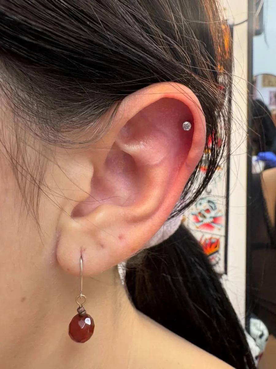 Crystal flat piercing on the upper ear cartilage with a dark red drop earring on the lobe