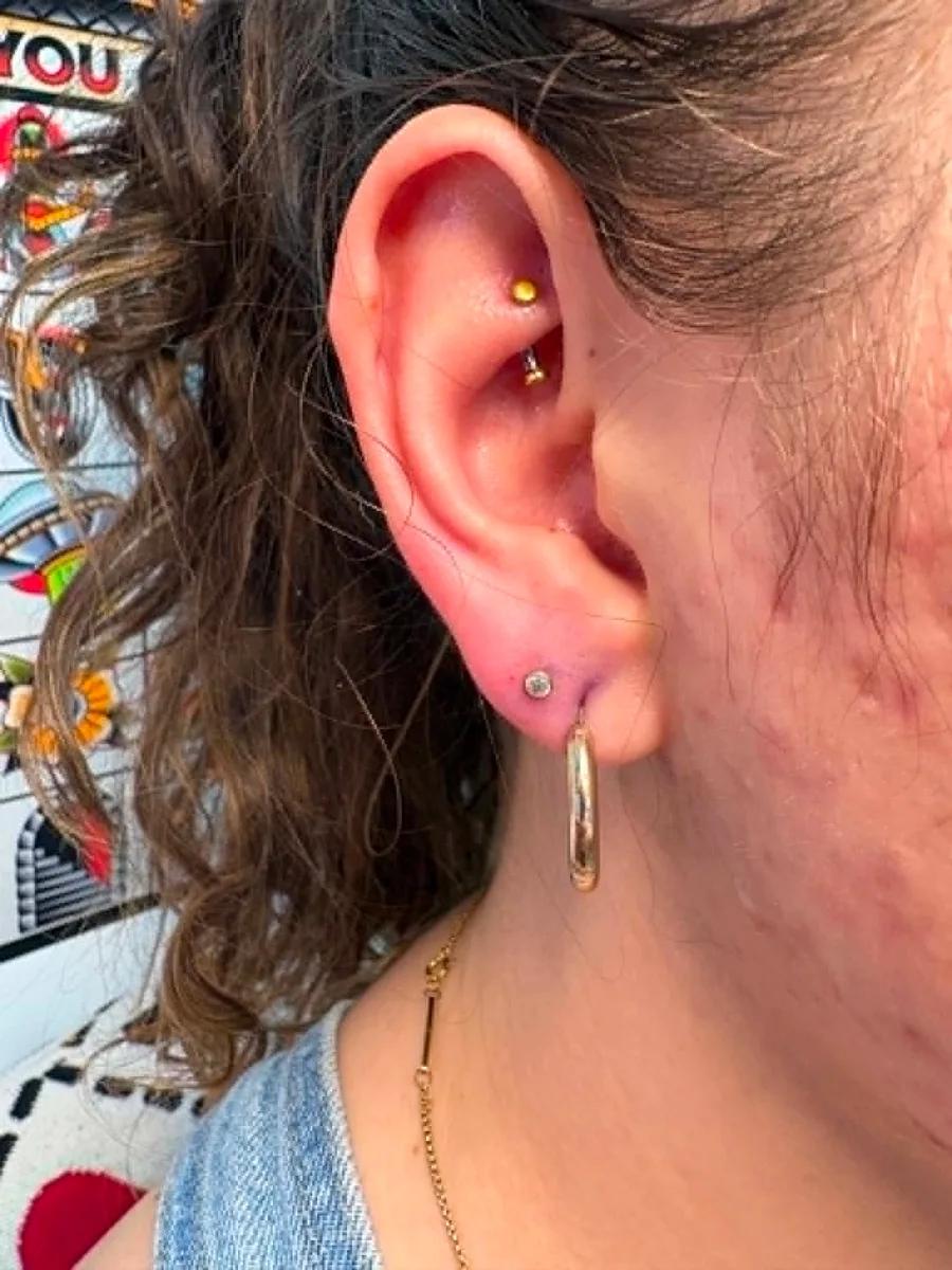 Rook piercing with a gold curved barbell above a lobe stud and hoop