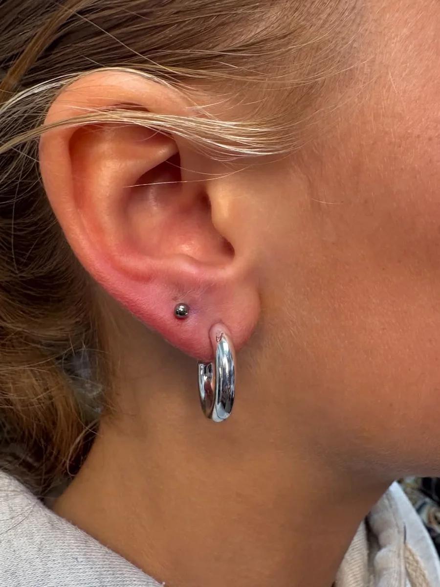 Fresh second lobe piercing with a small black ball stud above a chunky silver hoop