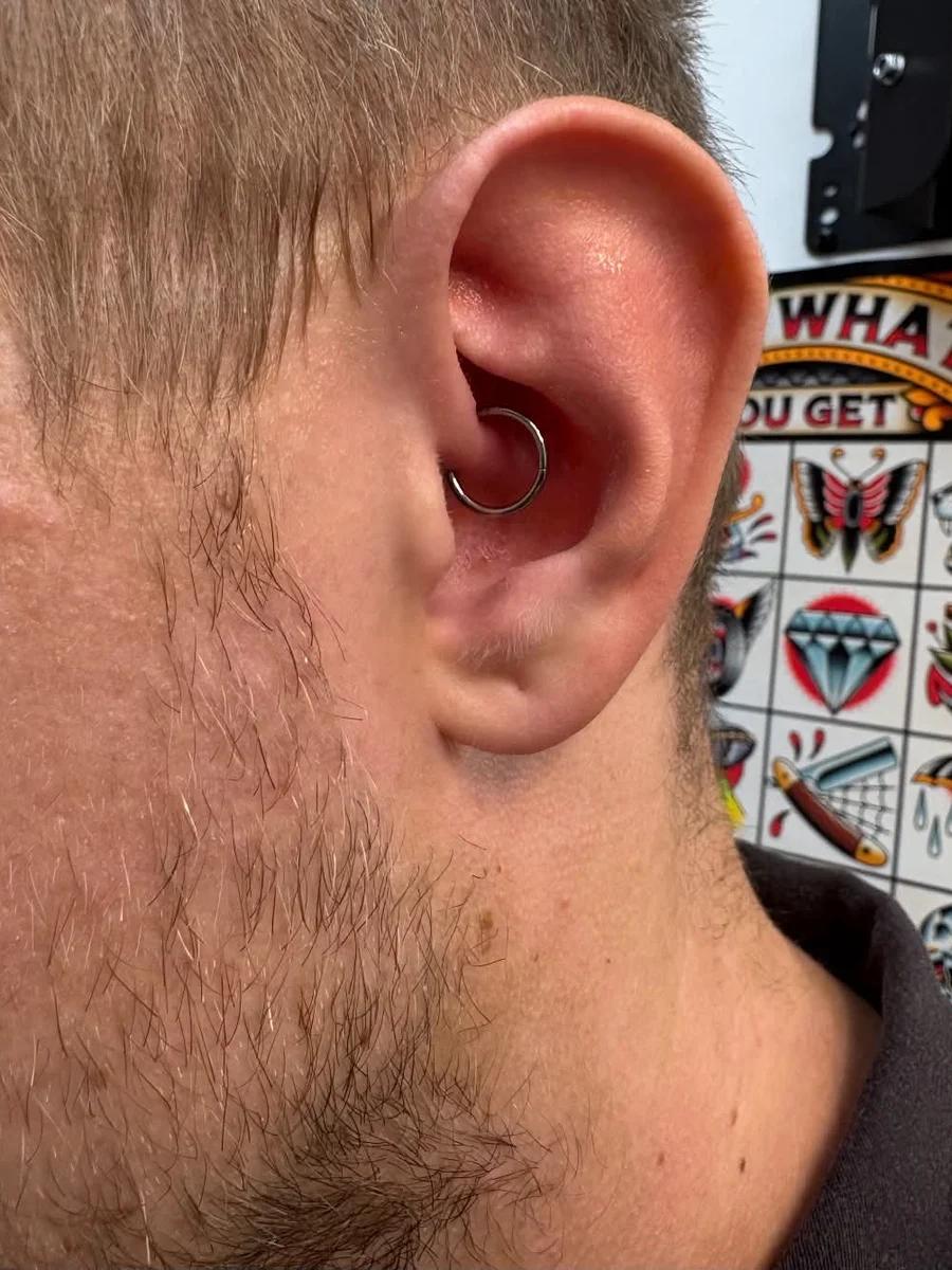 Daith piercing with a silver seamless ring, tattoo flash sheets on the wall behind