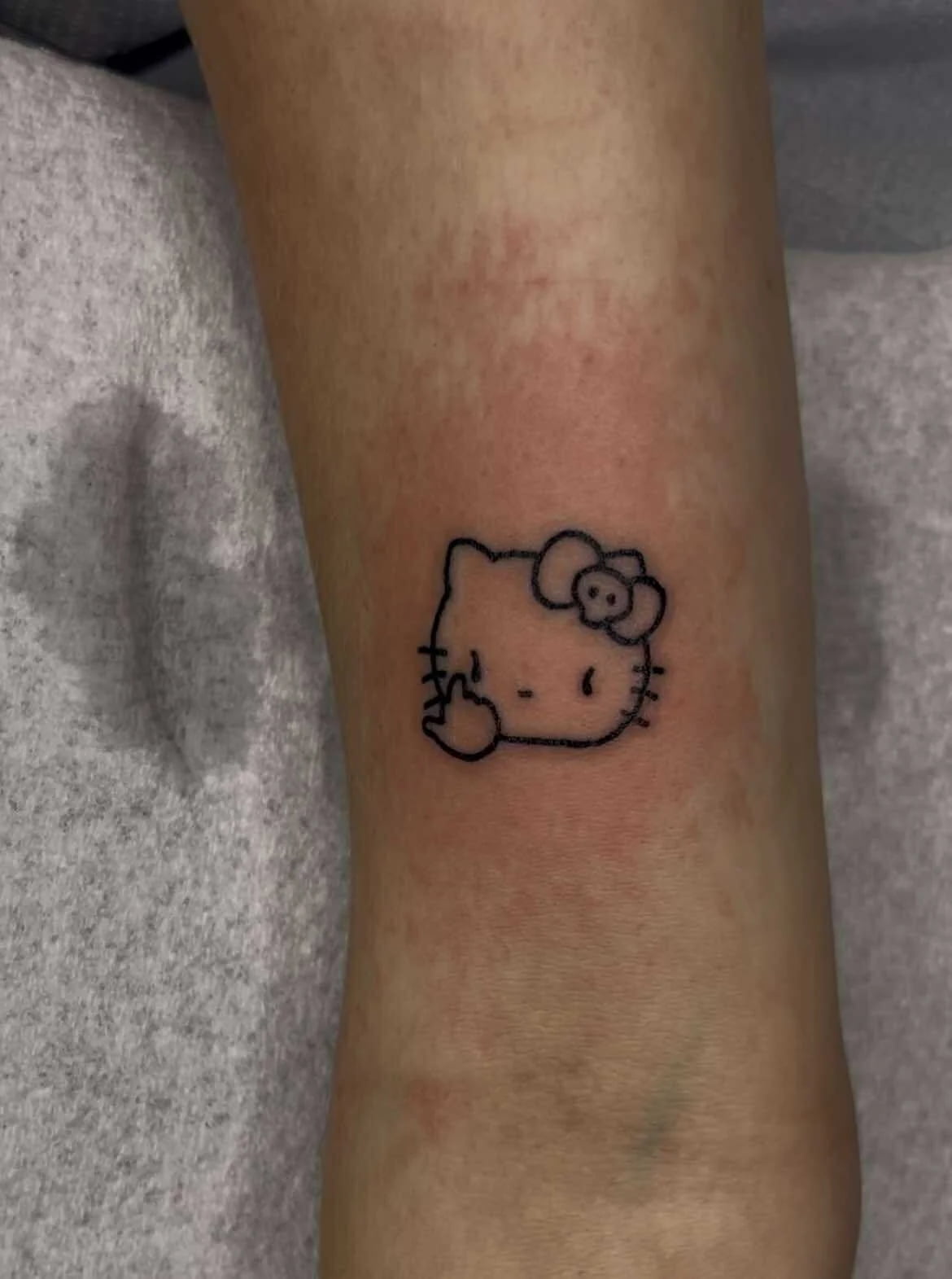 Fine line Hello Kitty tattoo with peace sign and minimalist character design