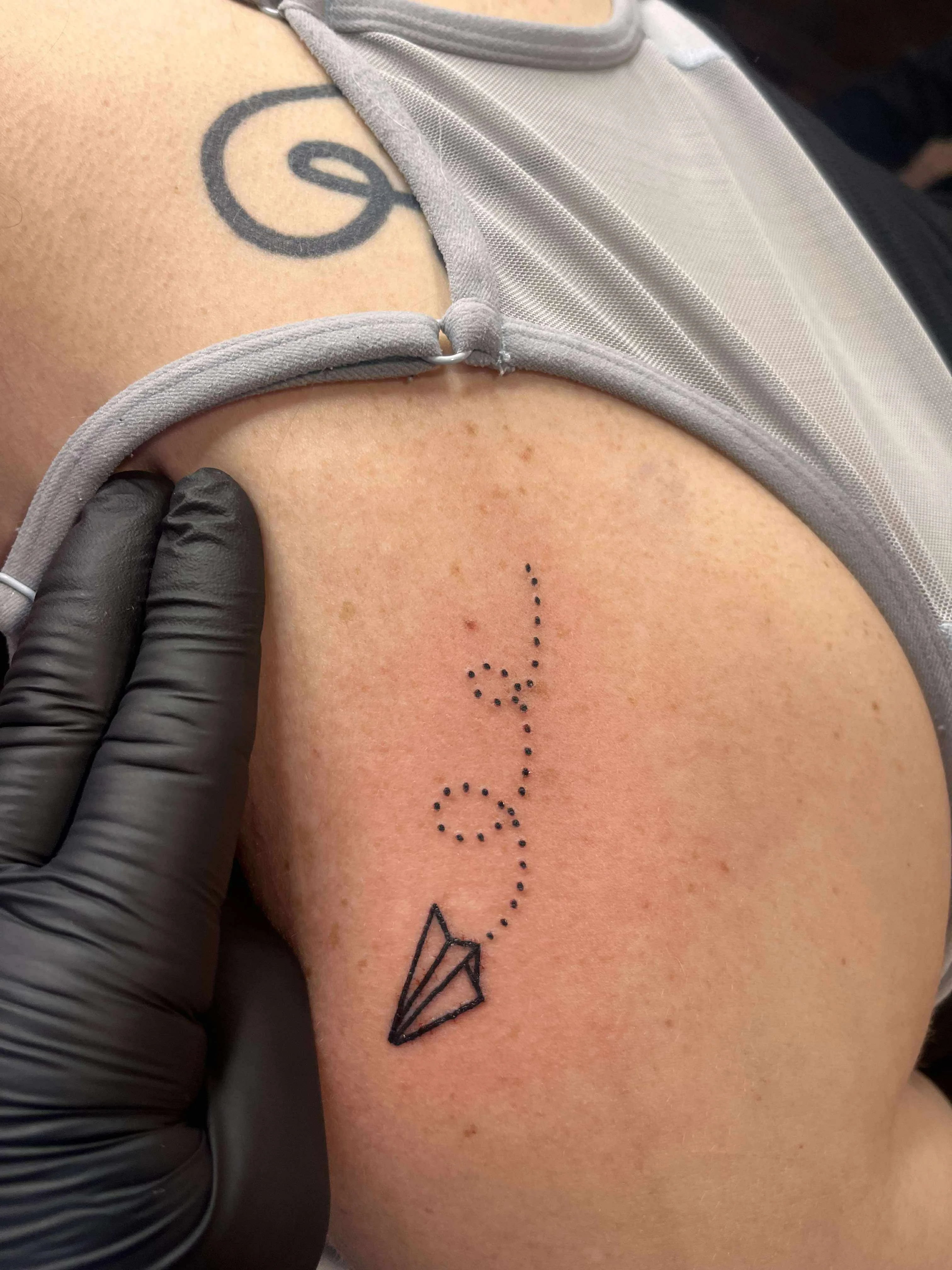 Fine line paper airplane tattoo with dotted flight path and simple design
