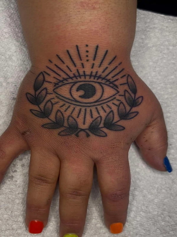 Traditional all-seeing eye tattoo on hand with radiating sunburst and decorative leaves