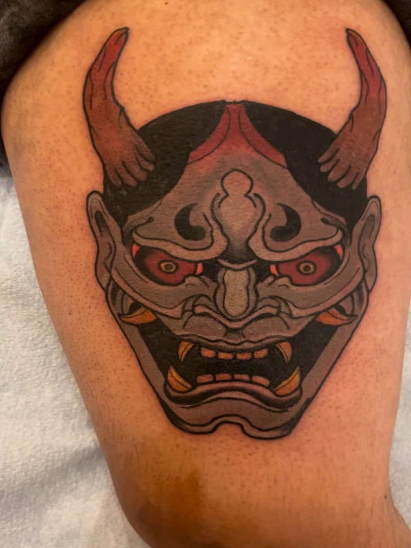 Traditional demon mask tattoo with bold lines and vibrant colors