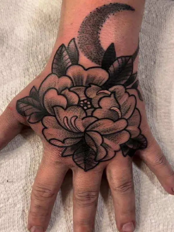 Traditional peony flower tattoo on hand with crescent moon and bold design