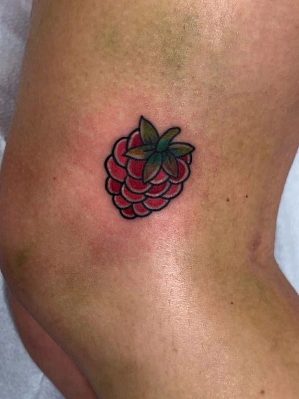 Traditional style raspberry tattoo with bold red berry and green leaves